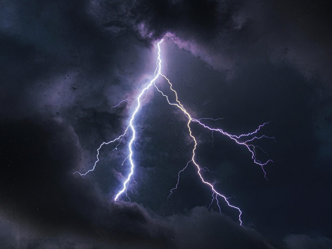 Close-up of a forked lightning bolt, white-blue core and violet edges in dark cloud.