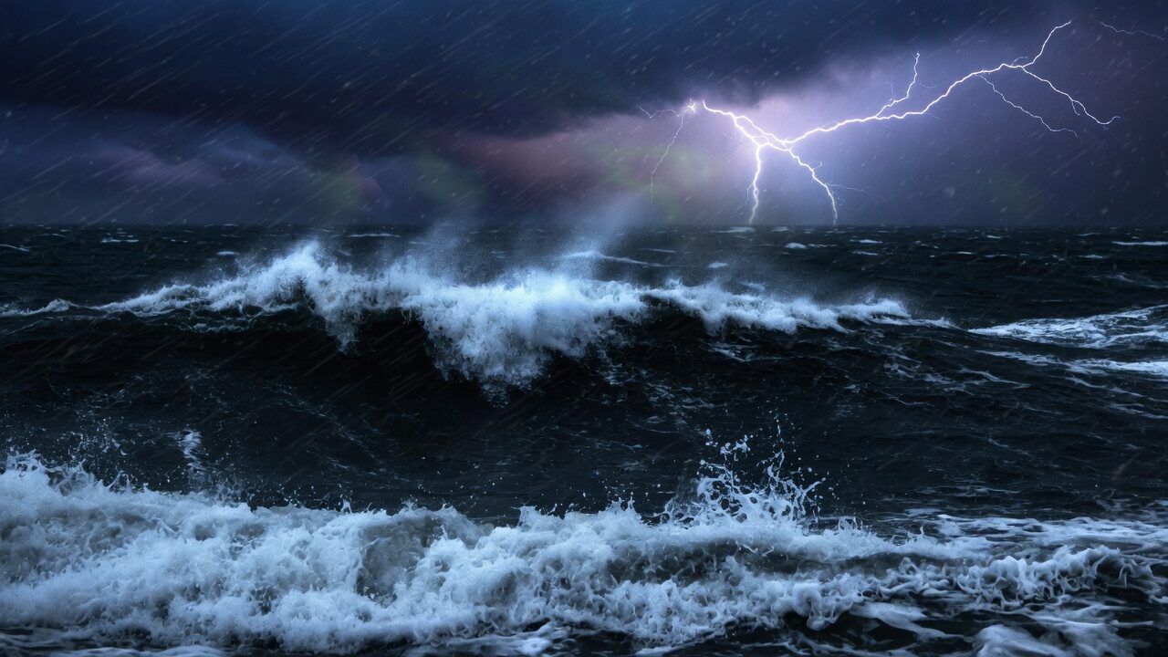 Storm ocean at night, white spray and a distant lightning flash.